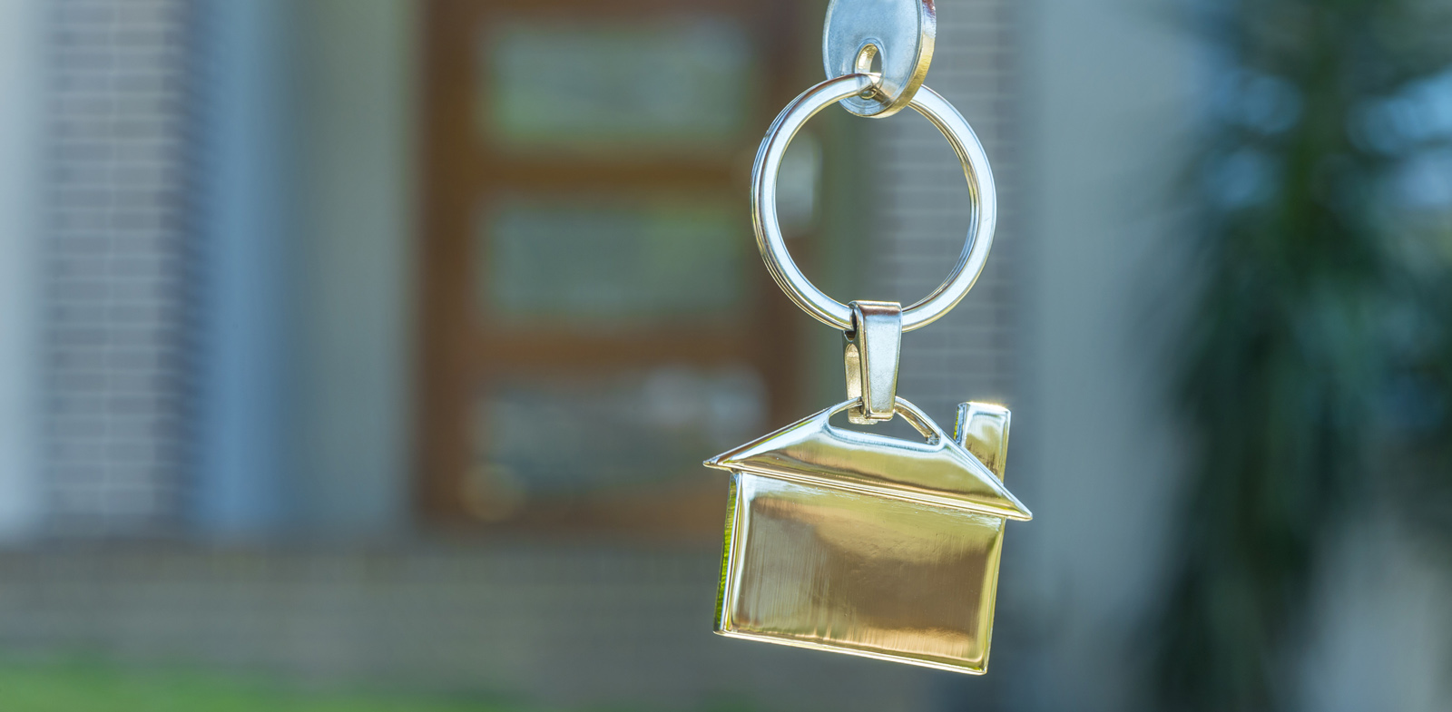 Hand holding a house key in front of a house. Slide Image #1